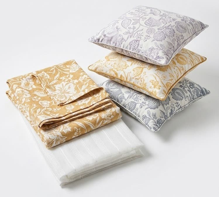 Floral print bedding and cushions in mustard, lilac and gray with folded white sheet