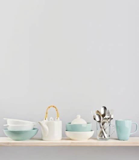 White and mint ceramic kitchenware set with cutlery on a wooden shelf