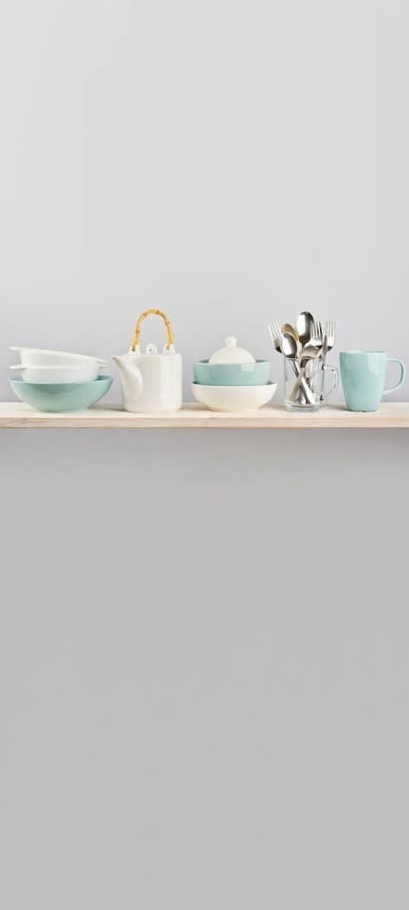White and mint ceramic kitchenware set with cutlery on a wooden shelf
