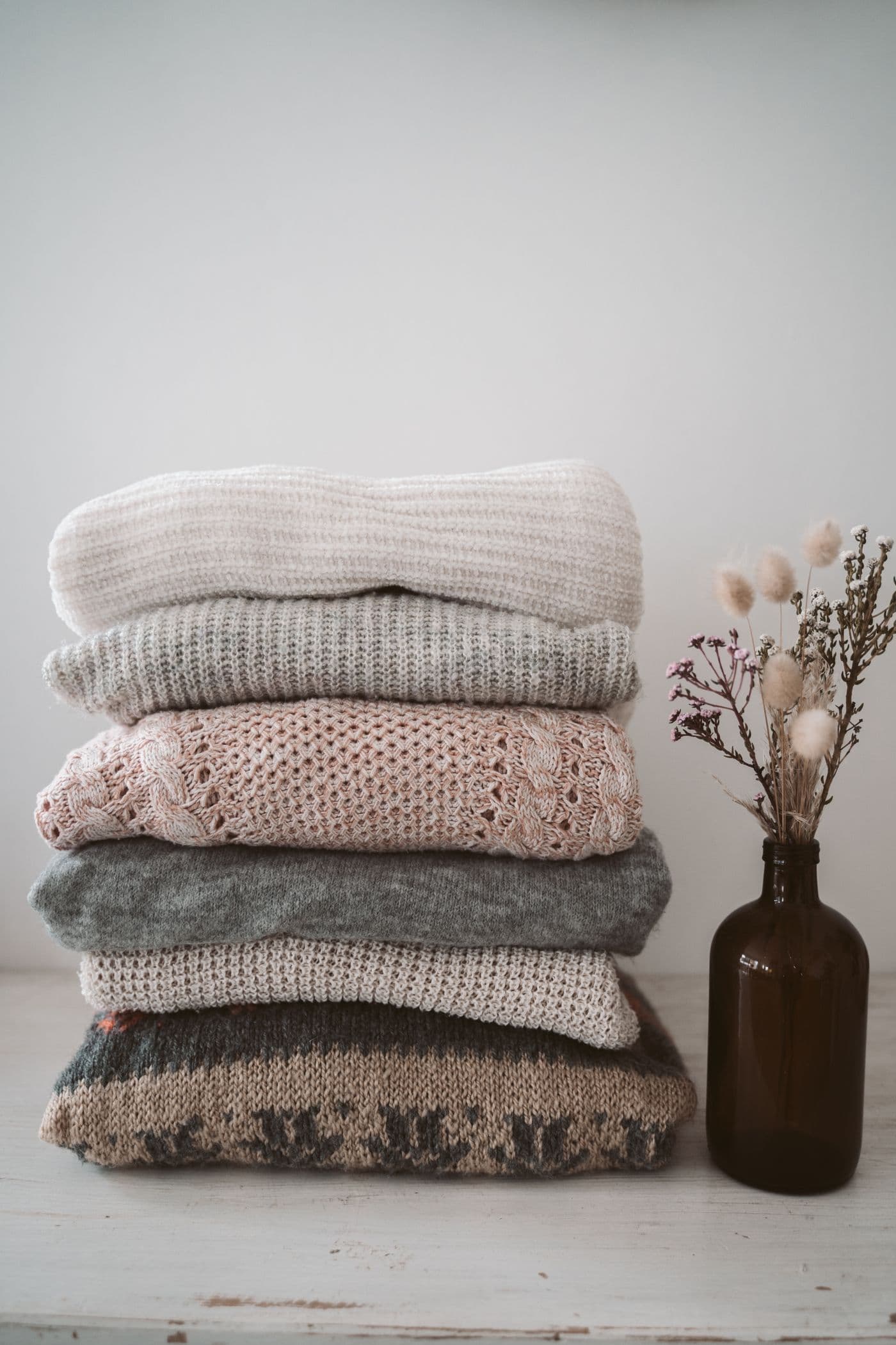 Stack of folded knit sweaters with dried flowers