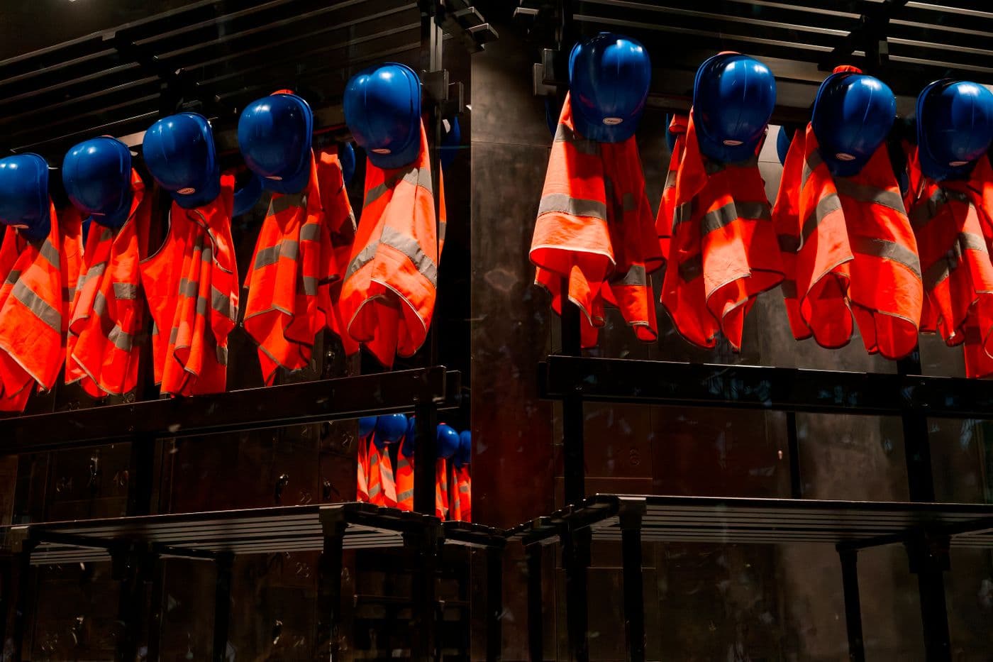 Row of orange safety vests and blue helmets hanging