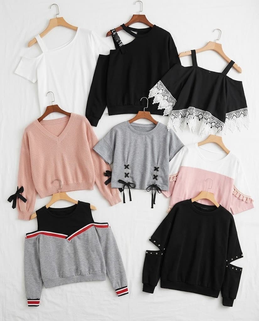 Assorted women's cold-shoulder and bow-detail tops on hangers in white, black, pink and grey